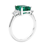 3 stone emerald cut diamond ring in modern gold setting with green gemstone center.