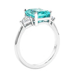 3 stone emerald cut diamond ring in modern gold setting with green gemstone center.