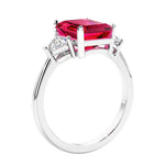 3 stone emerald cut diamond ring in modern gold setting with red gemstone center.