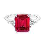 Three stone emerald cut engagement ring for timeless elegance featuring red gemstone and diamonds.