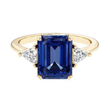 Emerald cut 3 stone engagement ring with blue gemstone and diamond accents.