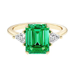Emerald cut 3 stone engagement ring with green gemstone and diamond accents.
