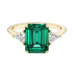 Emerald cut 3 stone engagement ring with green gemstone and diamond accents.