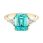 Emerald cut 3 stone engagement ring with green gemstone and diamond accents.