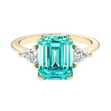 Emerald cut 3 stone engagement ring with green gemstone and diamond accents.