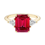 Emerald cut 3 stone engagement ring with red gemstone and diamond accents.