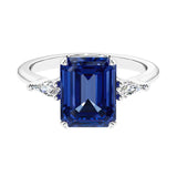 Three stone emerald cut engagement ring for timeless elegance featuring blue gemstone and diamonds.