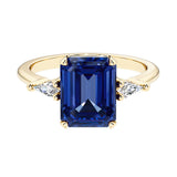 Emerald cut 3 stone engagement ring with blue gemstone and diamond accents.