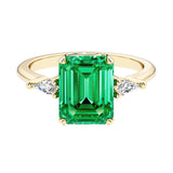 Emerald cut 3 stone engagement ring with green gemstone and diamond accents.