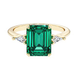 Emerald cut 3 stone engagement ring with green gemstone and diamond accents.