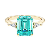 Emerald cut 3 stone engagement ring with green gemstone and diamond accents.