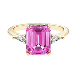 Emerald cut 3 stone engagement ring with pink gemstone and diamond accents.