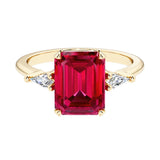 Emerald cut 3 stone engagement ring with red gemstone and diamond accents.