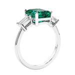 3 stone emerald cut diamond ring in modern gold setting with green gemstone center.