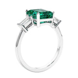 3 stone emerald cut diamond ring in modern gold setting with green gemstone center.