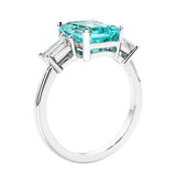 3 stone emerald cut diamond ring in modern gold setting with green gemstone center.