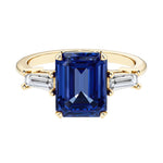 Emerald cut 3 stone engagement ring with blue gemstone and diamond accents.
