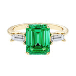 Emerald cut 3 stone engagement ring with green gemstone and diamond accents.