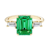 Emerald cut 3 stone engagement ring with green gemstone and diamond accents.