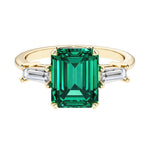 Emerald cut 3 stone engagement ring with green gemstone and diamond accents.
