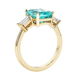 Emerald cut 3 diamond ring representing past, present, and future featuring green gemstone center.