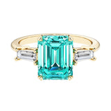Emerald cut 3 stone engagement ring with green gemstone and diamond accents.