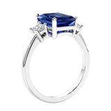 3 stone emerald cut diamond ring in modern gold setting with blue gemstone center.