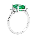 3 stone emerald cut diamond ring in modern gold setting with green gemstone center.
