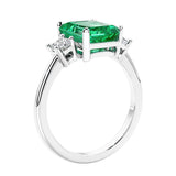 3 stone emerald cut diamond ring in modern gold setting with green gemstone center.
