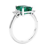 3 stone emerald cut diamond ring in modern gold setting with green gemstone center.