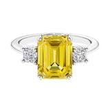 Three stone emerald cut engagement ring for timeless elegance featuring yellow gemstone and diamonds.
