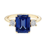 Emerald cut 3 stone engagement ring with blue gemstone and diamond accents.