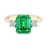 Emerald cut 3 stone engagement ring with green gemstone and diamond accents.
