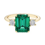 Emerald cut 3 stone engagement ring with green gemstone and diamond accents.