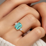 Woman wearing emerald cut three stone engagement ring with bold lines.