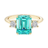 Emerald cut 3 stone engagement ring with green gemstone and diamond accents.