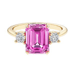 Emerald cut 3 stone engagement ring with pink gemstone and diamond accents.