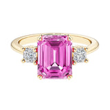 Emerald cut 3 stone engagement ring with pink gemstone and diamond accents.