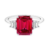 Three stone emerald cut engagement ring for timeless elegance featuring red gemstone and diamonds.