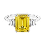 Three stone emerald cut engagement ring for timeless elegance featuring yellow gemstone and diamonds.
