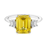 Three stone emerald cut engagement ring for timeless elegance featuring yellow gemstone and diamonds.