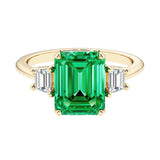 Emerald cut 3 stone engagement ring with green gemstone and diamond accents.