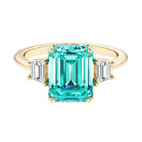Emerald cut 3 stone engagement ring with green gemstone and diamond accents.