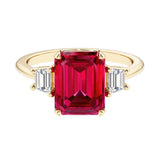 Emerald cut 3 stone engagement ring with red gemstone and diamond accents.