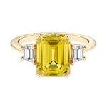 Emerald cut 3 stone engagement ring with yellow gemstone and diamond accents.