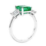 3 stone emerald cut diamond ring in modern gold setting with green gemstone center.