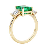 Emerald cut 3 diamond ring representing past, present, and future featuring green gemstone center.