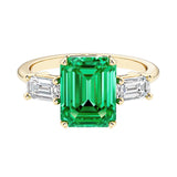 Emerald cut 3 stone engagement ring with green gemstone and diamond accents.