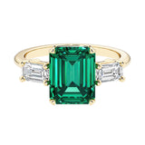 Emerald cut 3 stone engagement ring with green gemstone and diamond accents.
