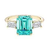 Emerald cut 3 stone engagement ring with green gemstone and diamond accents.